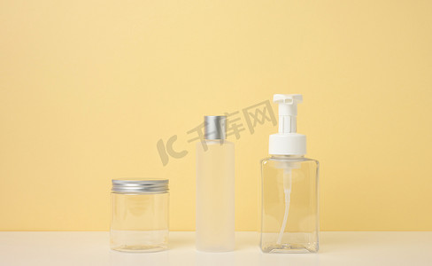 奶油管、化妆品分配器、空塑料罐、浅黄色背景上的透明分配器。