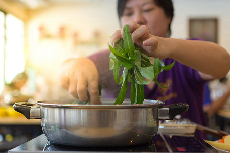 亚洲女人把蔬菜放进火锅里做饭