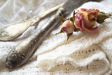 餐具刀和叉摄影照片_白色复古餐巾和干玫瑰上带刀的旧银叉