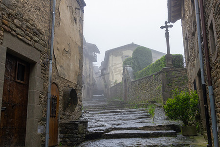古代街道摄影照片_雨中 Rupit 的街道，可见石十字架