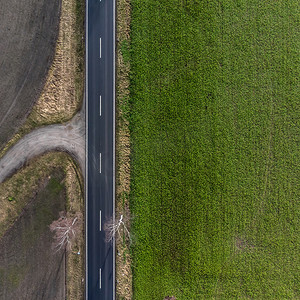 德国一条柏油乡村道路的鸟瞰图，左侧是农田，右侧是绿色草地。