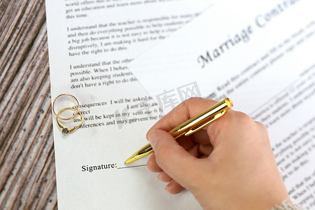 与两个金婚戒指和金笔的婚姻合同、婚前协议、宏观特写、签字、文件、协议概念