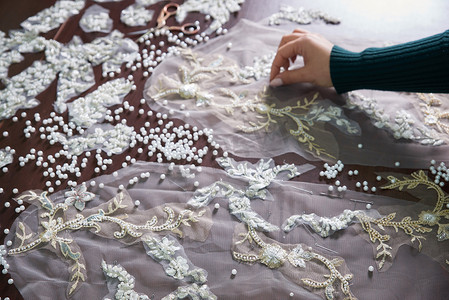 工作室里裁缝用珠子和蕾丝缝制婚纱的女手特写