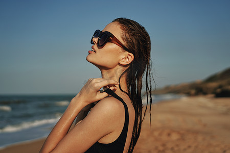 穿着黑色泳衣太阳镜的快乐女人海滩散步旅行