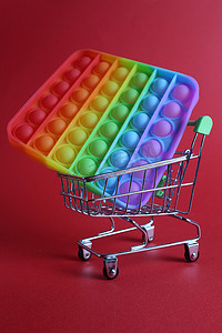 这款多色玩具是一个简单的酒窝抗压玩具，放在一篮子婴儿车购物车中，红色背景，有文字复制空间。