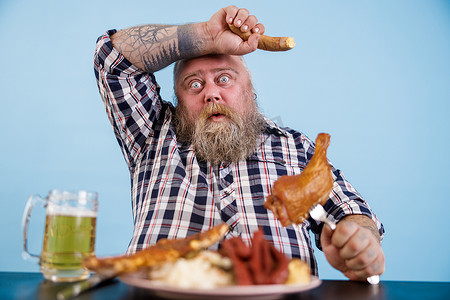疲惫的肥胖男子在工作室里用脂肪食物擦拭餐桌上暴饮暴食的眉毛
