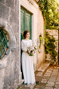 微笑的新娘站在建筑物的背景下，手里拿着一束美丽的鲜花