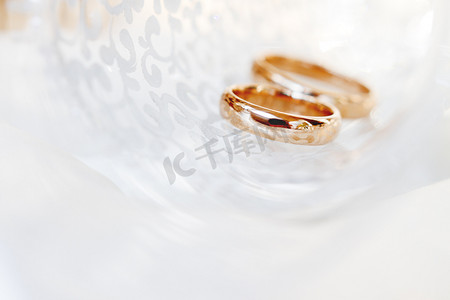结婚金色摄影照片_在透明玻璃中的结婚金戒指。