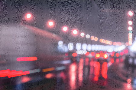 雨中街道摄影照片_行驶中的汽车和灯笼的模糊灯光反射在夜城被雨覆盖的窗户后面潮湿的沥青上。