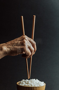 简约的老手抓着日本筷子，越过一碗米饭概念，在黑色背景下以电影色调拍摄