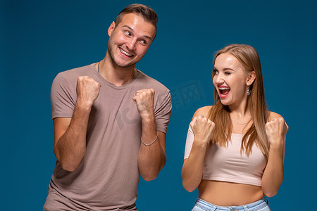 拳头背景摄影照片_喜出望外的女人和男人胜利地举起拳头，达成成功的交易，在蓝色背景下欢呼雀跃。