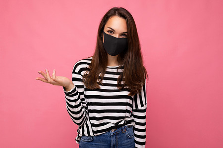 年轻漂亮的女人，脸上戴着可重复使用的病毒防护面罩，抵御粉色背景墙上隔离的冠状病毒