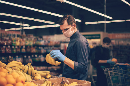 戴着防护手套的男子在超市挑选香蕉。