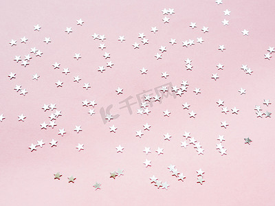 假日背景与粉红色背景上的银色星星五彩纸屑。