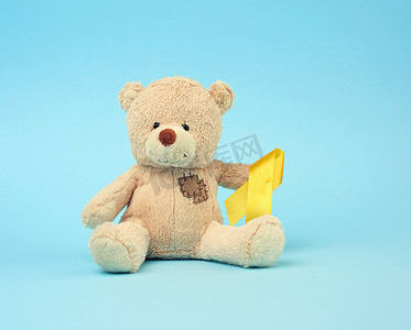 带补丁的可爱棕色泰迪熊在里面拿着一条丝绸黄色丝带