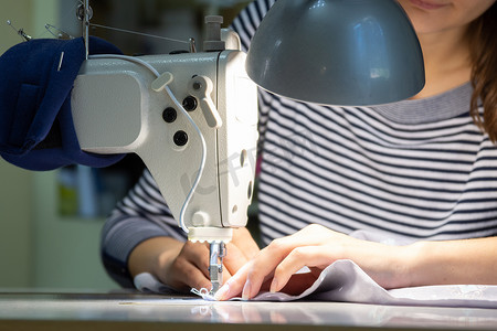 裁缝工作摄影照片_在缝纫机上工作的女孩的手的特写