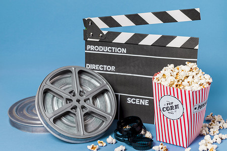 电影爆米花可乐摄影照片_电影卷轴电影条拍板与爆米花盒蓝色背景。