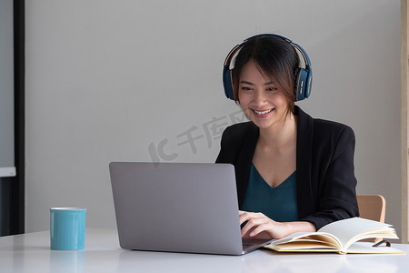 快乐的亚洲女性戴着耳机笑，使用笔记本电脑视频流电话会议在线教学，快乐的民族女学生游戏玩家导师玩得开心观看网络研讨会网络摄像头教育娱乐概念