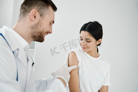 医生用听诊器向一名女病人的肩膀注射新冠疫苗