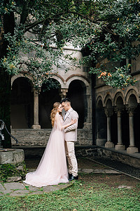 新郎拥抱新娘，站在意大利科莫湖一座有柱子的老别墅背景下的绿色花园里