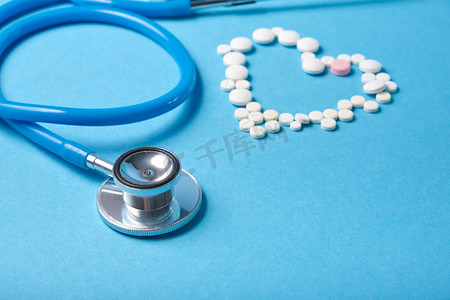 蓝色背景药丸中的听诊器和心脏，心脏病学概念