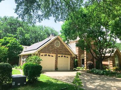 美国德克萨斯州达拉斯郊区典型的单户住宅，太阳能电池板屋顶被高大的树木环绕