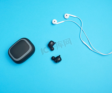 耳机充电摄影照片_蓝色背景上带电线的黑色无线和白色耳机