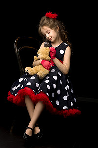 女孩抱着摄影照片_穿着圆点连衣裙的可爱女孩抱着一只泰迪熊