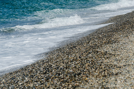 蓝色海浪装饰摄影照片_被海浪冲刷的卵石海滩，形成海岸的小而各种各样的石头