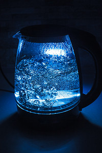 黑茶壶摄影照片_黑色 backgr 上带蓝色背光的沸腾玻璃黑茶壶