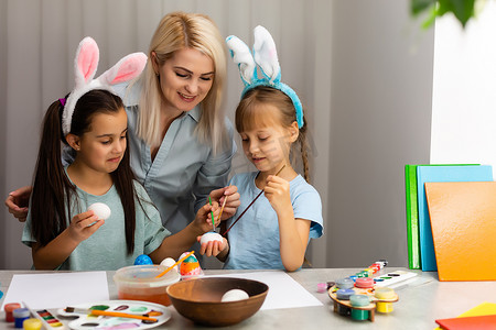 年轻的母亲和她的两个小女儿在家画色彩缤纷的复活节彩蛋