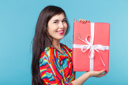开朗漂亮的年轻黑发女人手里拿着一个红色礼品盒，但背景是蓝色的。