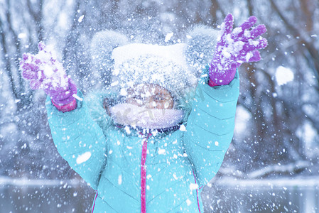冬天冷的人摄影照片_一个穿着木炭夹克的小女孩冬天在街上玩雪。孩子们在冬天在外面玩耍。