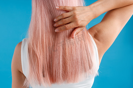 特写镜头中，一位女性在蓝色工作室背景下摆出孤立的姿势，抚摸着光滑自然的粉红色长发
