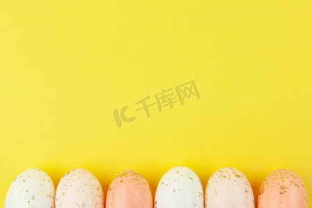 用金箔装饰的柔和色彩的创意彩蛋沿着黄色背景的底部边缘排成一排，复制空间。