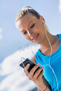 在公园里用智能手机听音乐时站着的年轻漂亮女人的画像