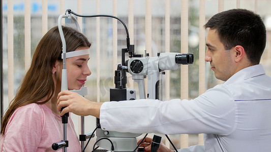 眼科治疗 — 年轻微笑的女人用明亮柜子里的特殊设备检查她的视力 — 把她的下巴放在立场上