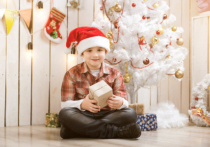 小男孩坐在新年树附近的地板上