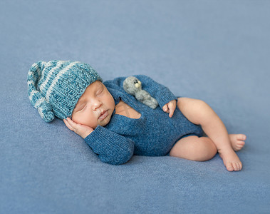 穿着蓝色连衣裤和帽子睡觉的新生婴儿