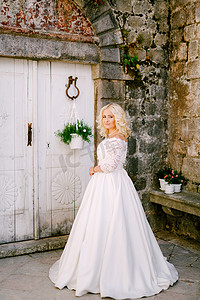 佩拉斯特，一位新娘站在一栋旧砖房前，靠近一扇白色木门，门上放着花盆
