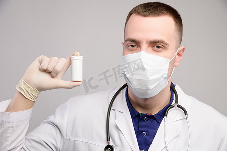 戴着面具和白大褂的年轻白人医生手里拿着一个装有未知药丸的包裹。