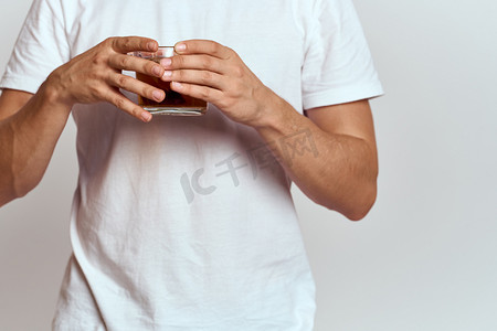 一个男人手里拿着一杯热茶，穿着白色 T 恤，背景是浅色的裁剪视图
