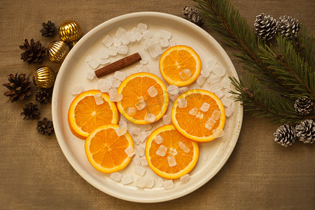 金球摄影照片_圣诞树枝、金球和松果附近盘子里的橙子。