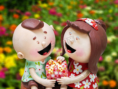 男孩女孩礼物摄影照片_陶瓷娃娃男孩女孩和手上的礼物花园黑色