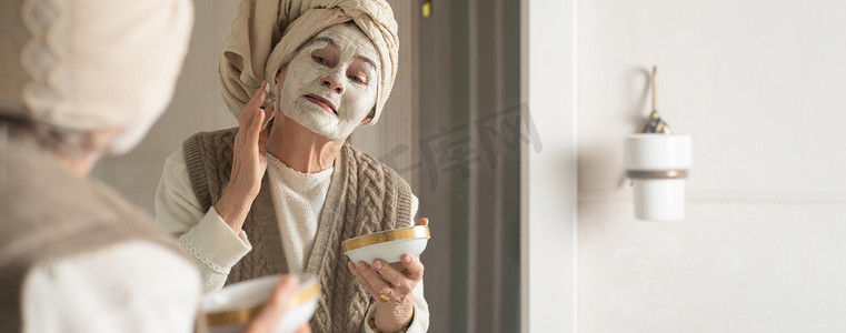 头上戴着毛巾的老妇人微笑着，敷上清洁面膜。