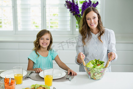 微笑的母女在厨房里搅拌碗沙拉的画像