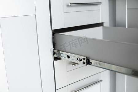 带抽屉电视柜摄影照片_不锈钢伸缩卡口抽屉滑轨，安装在灰色刨花板上的厨柜上。