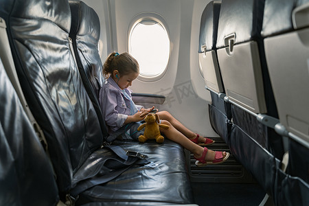 乘飞机旅行摄影照片_乘飞机旅行时，小女孩坐在椅子上玩手机