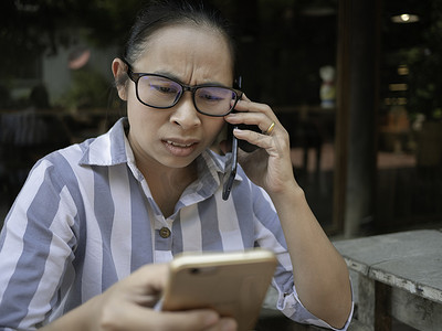 在咖啡厅打电话时，压力重重的亚洲年轻女性拿着智能手机上班，脸上不快乐而严肃。
