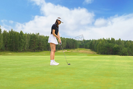 美丽的女高尔夫球手准备在绿色高尔夫球场上击球。